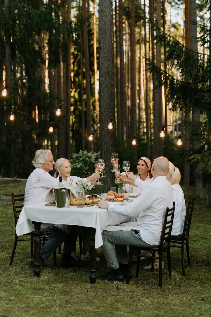 A group of friends toasting in a cheerful outdoor dinner setting surrounded by nature.